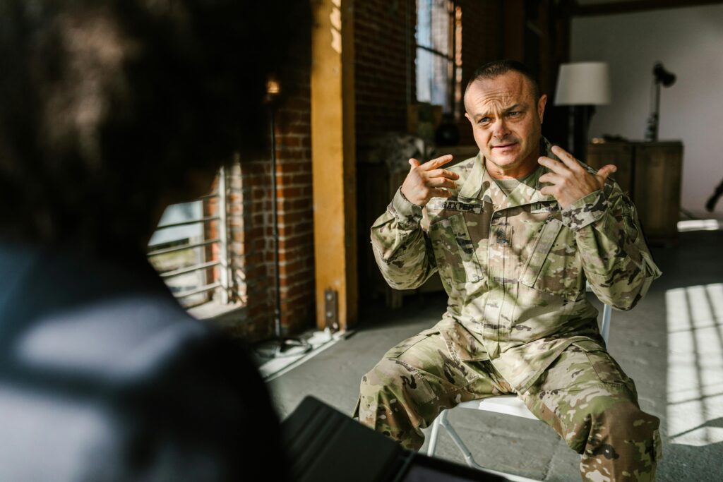 A combat veteran in military uniform engages in a counseling session indoors, expressing emotions.