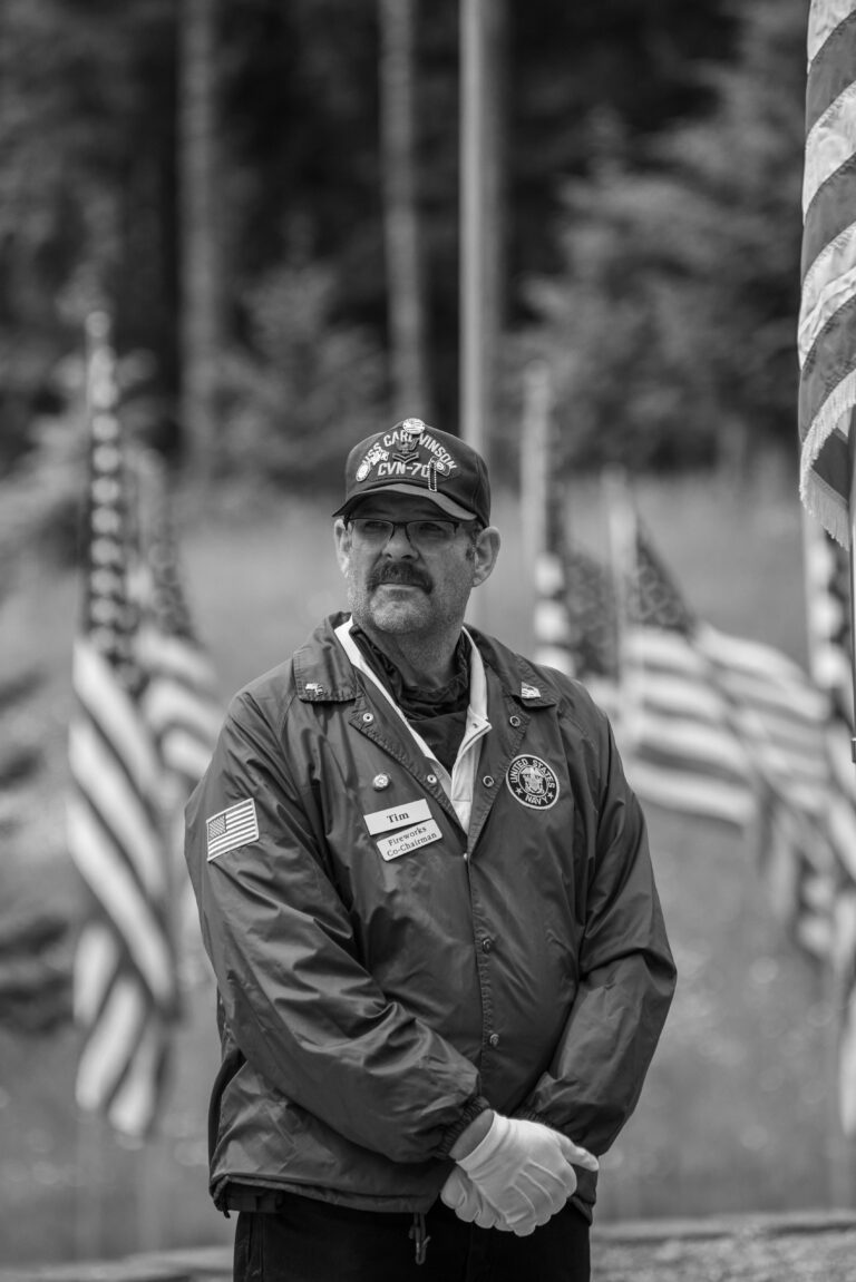 A solemn portrait of a veteran in uniform during a memorial ceremony, surrounded by American flags.